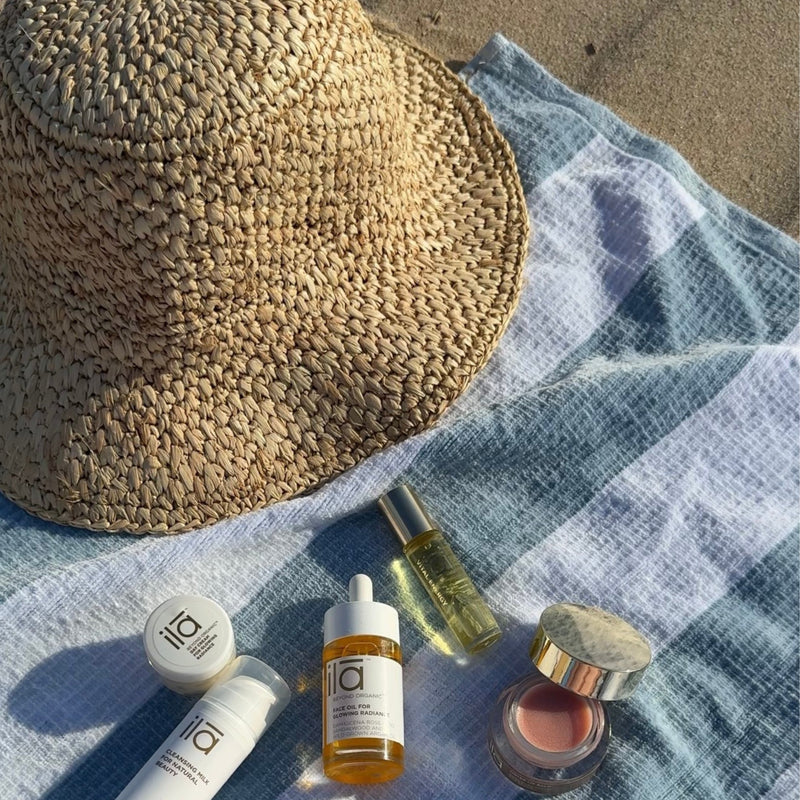 ila skincare products lay on a blue and white striped beach towel